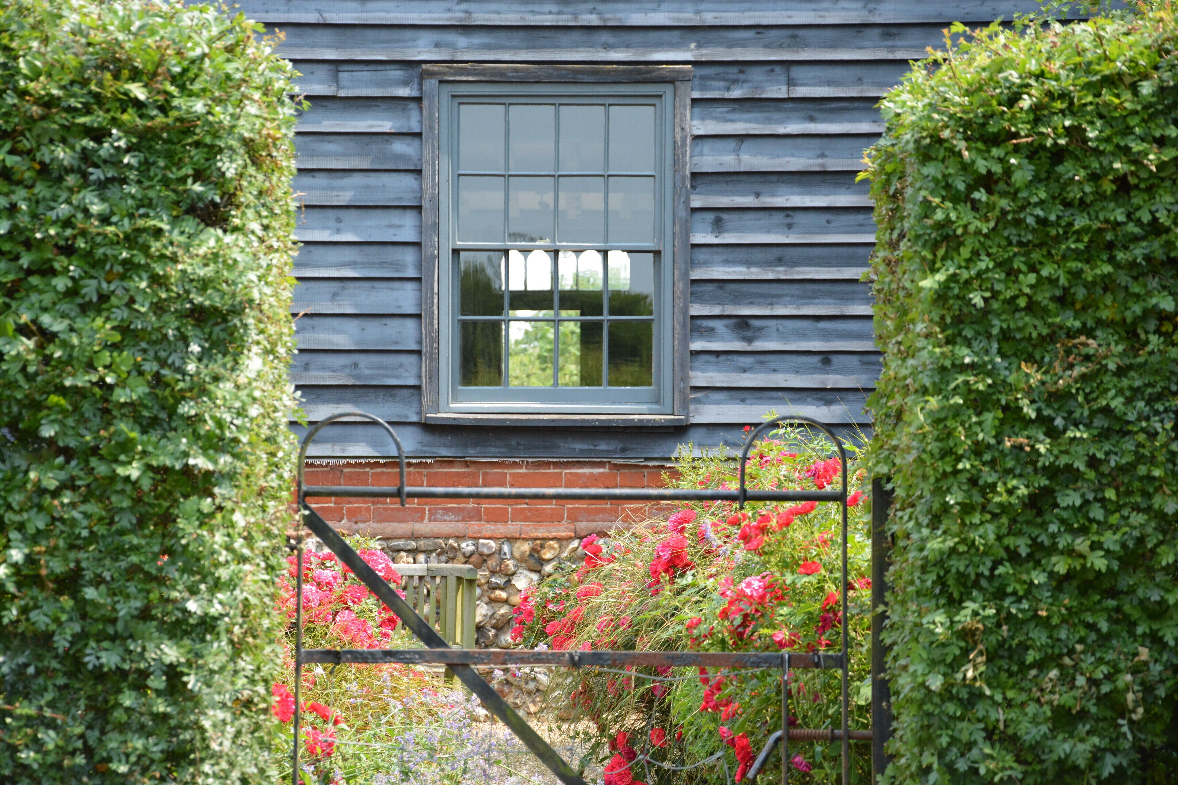 Et træhus med et vindue og en port omgivet af frodig vegetation og farverige blomster.