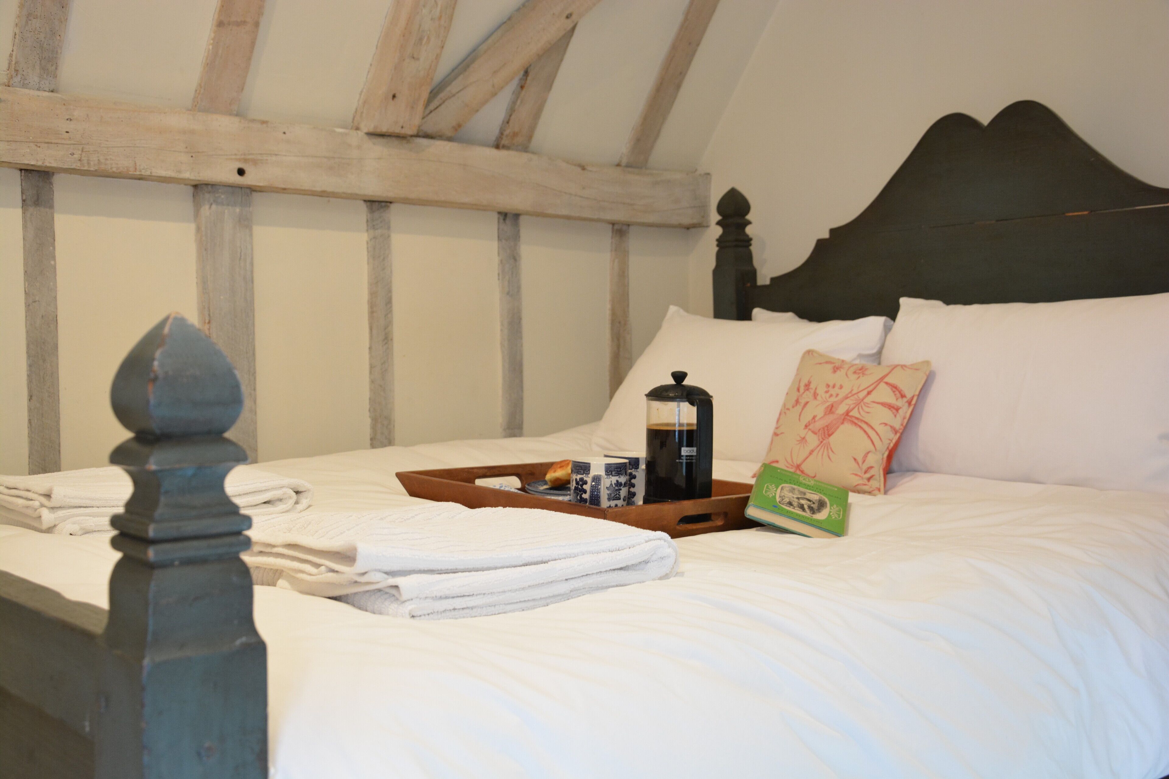 A neatly made bed with a tray of breakfast items, a pillow, and a bedside table.