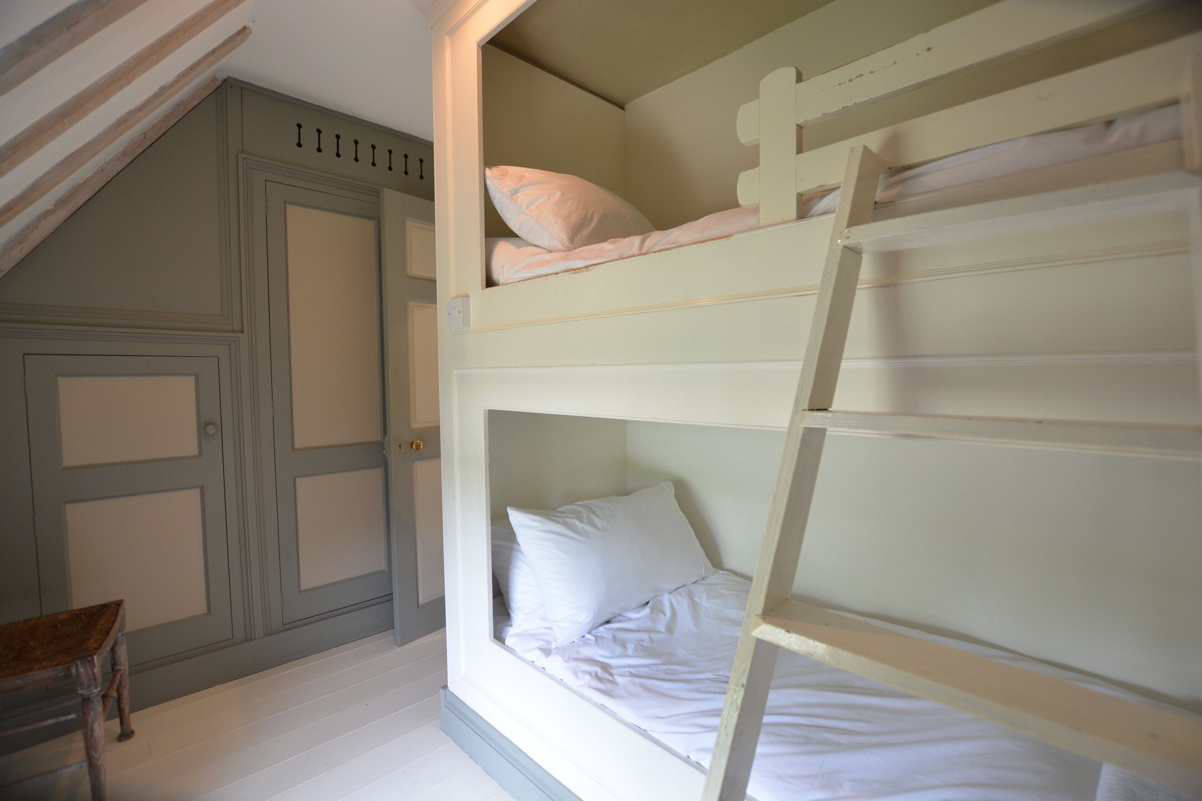 Una cama litera con una escalera, una silla de madera y una puerta con paneles.