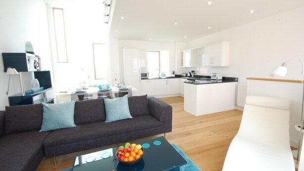 A modern living room with a dark grey sofa, a coffee table with fruit, and a white armchair. - Seal Cove (Reydon)