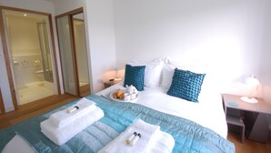 A hotel room with a bed, a bedside table with a lamp, a tray with croissants and coffee cups, and a shower area. - Seal Cove (Reydon)