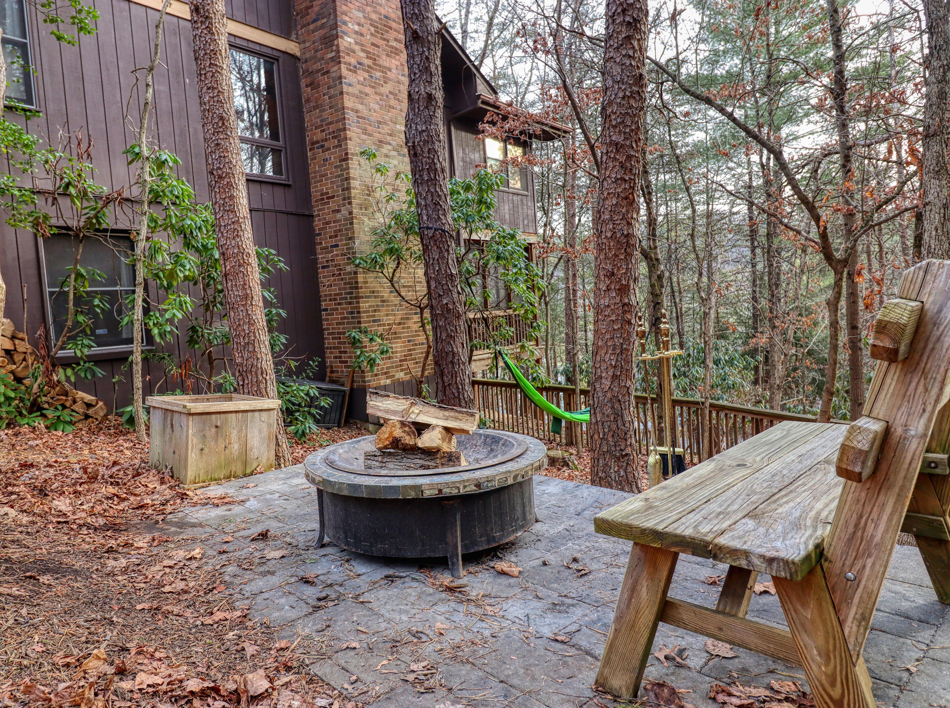 A wooden deck with a circular fire pit, a bench, and a hammock.