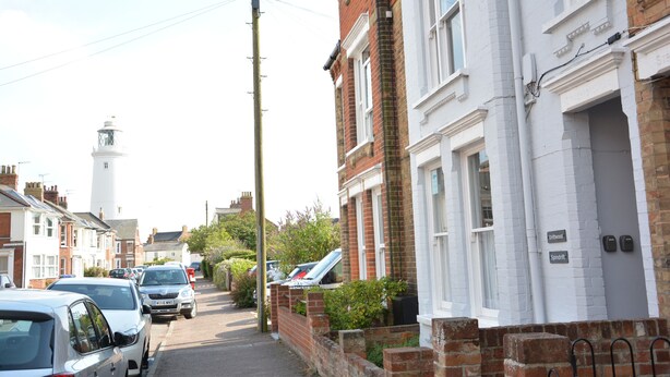 A narrow residential street lined with terraced houses, a white tower, and parked cars. - Spindrift, Southwold (Reydon)