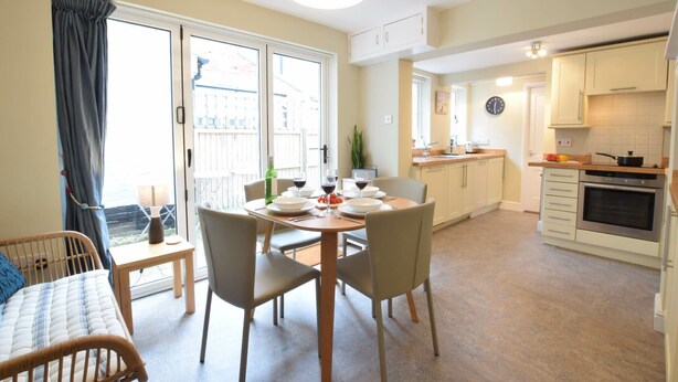 A modern apartment with a dining area, kitchen, and a balcony with curtains. - Spindrift, Southwold (Reydon)