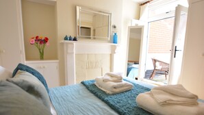 A bedroom with a bed, a blue blanket, and a stack of towels. - Spindrift, Southwold (Reydon)