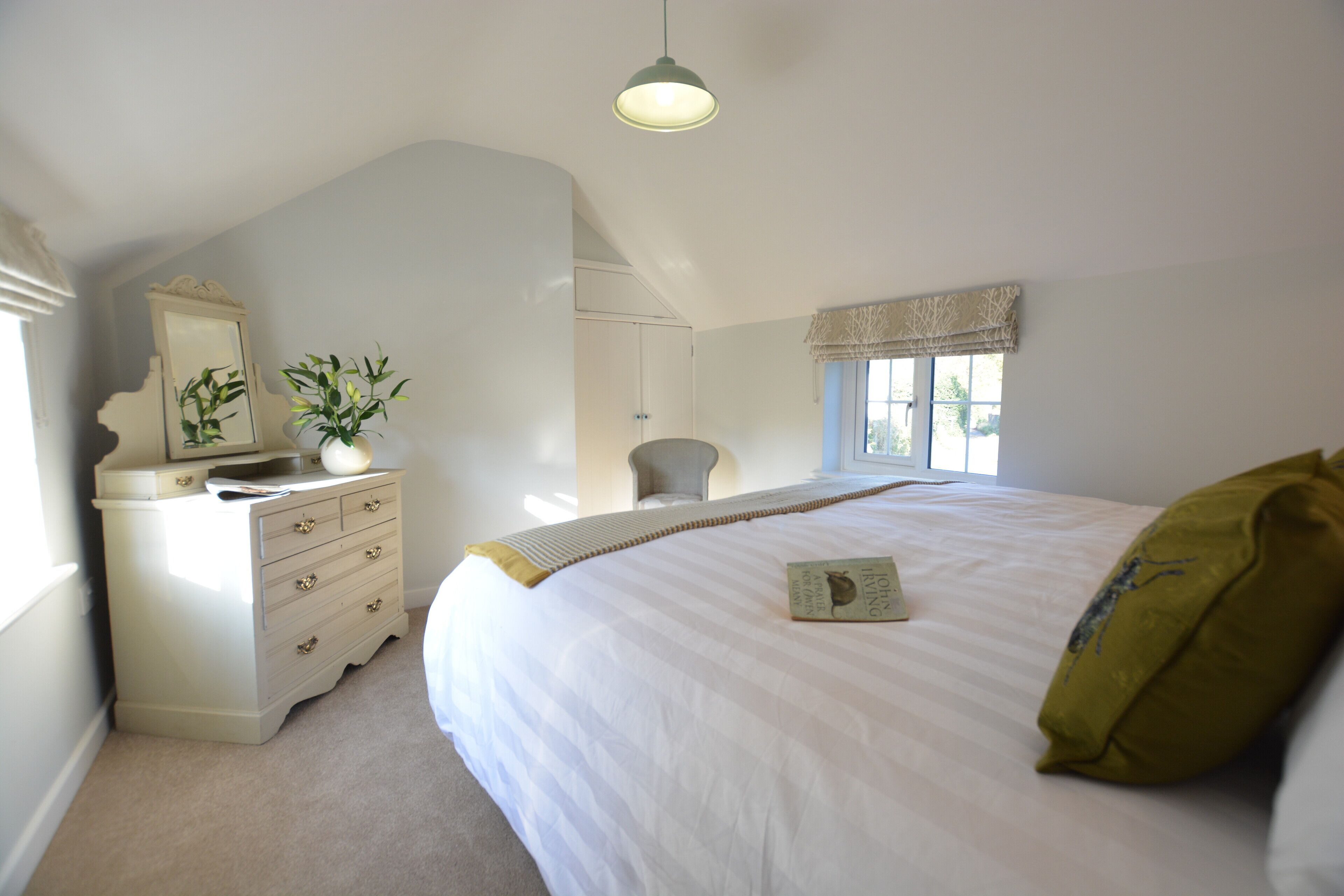 A bedroom with a large bed, a dresser, a chair, and a window with curtains.