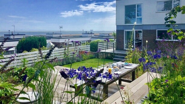 A modern building with a large window, a patio with a table set for a meal, and a view of the sea.