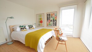 A bedroom with a bed, a desk, a chair, a floor lamp, and two wall art pieces.