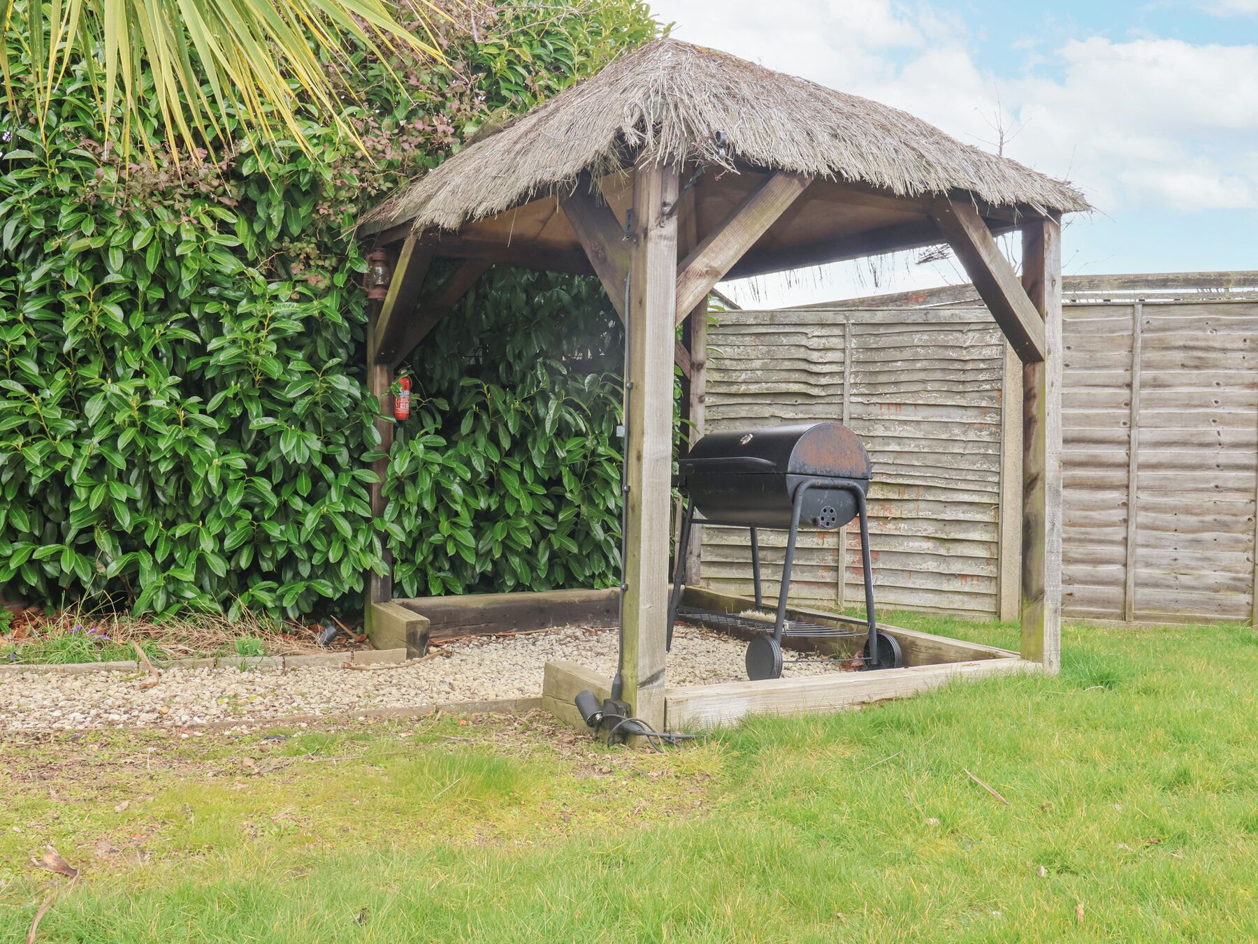 Un abri en bois pour barbecue, doté d’un toit de chaume, d’un gril et d’un tuyau d’arrosage.