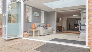 Un salon moderne avec un canapé, une table basse et des objets décoratifs. Une porte vitrée donne sur l’extérieur.
