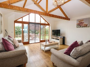 A spacious living room with a large sliding glass door leading to an outdoor patio, a television on a white stand, and a painting of a cow on the wall. - The Mulberry, nr Bungay (Beccles)