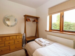 A bedroom with a wooden dresser, a bed with a white comforter, a wooden wardrobe, a mirror, and a window with a view of greenery. - The Mulberry, nr Bungay (Beccles)