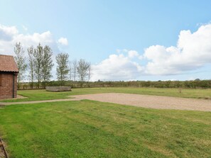 A grassy outdoor area with a brick building, a gravel path, and a fence. - The Mulberry, nr Bungay (Beccles)