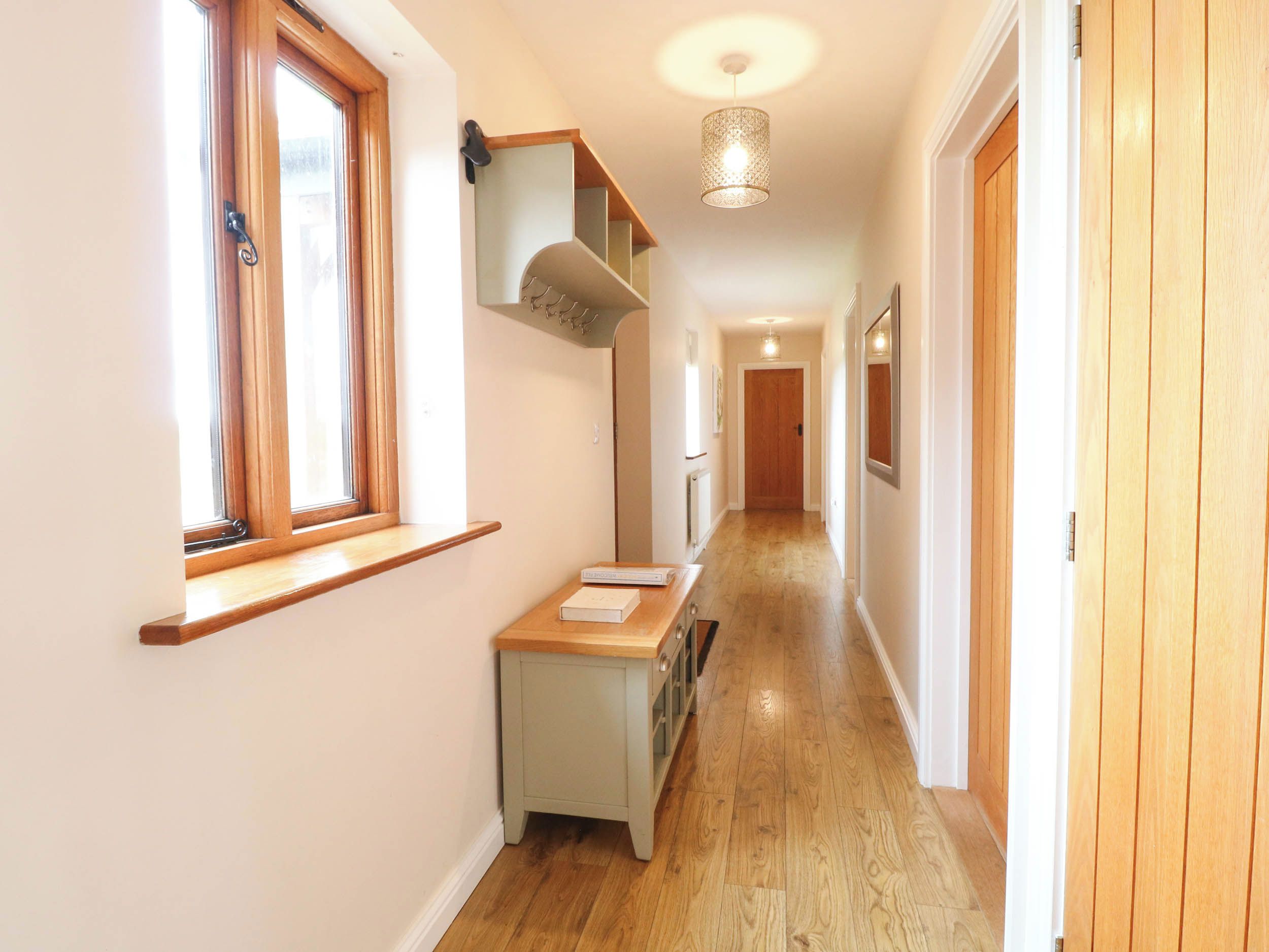 A hallway with wooden flooring, a built-in bench, a hanging light fixture, and a door at the end.