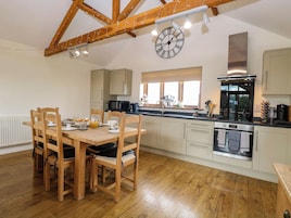 A modern kitchen with wooden beams, a large clock, and a dining area with wooden chairs and a table set for breakfast.