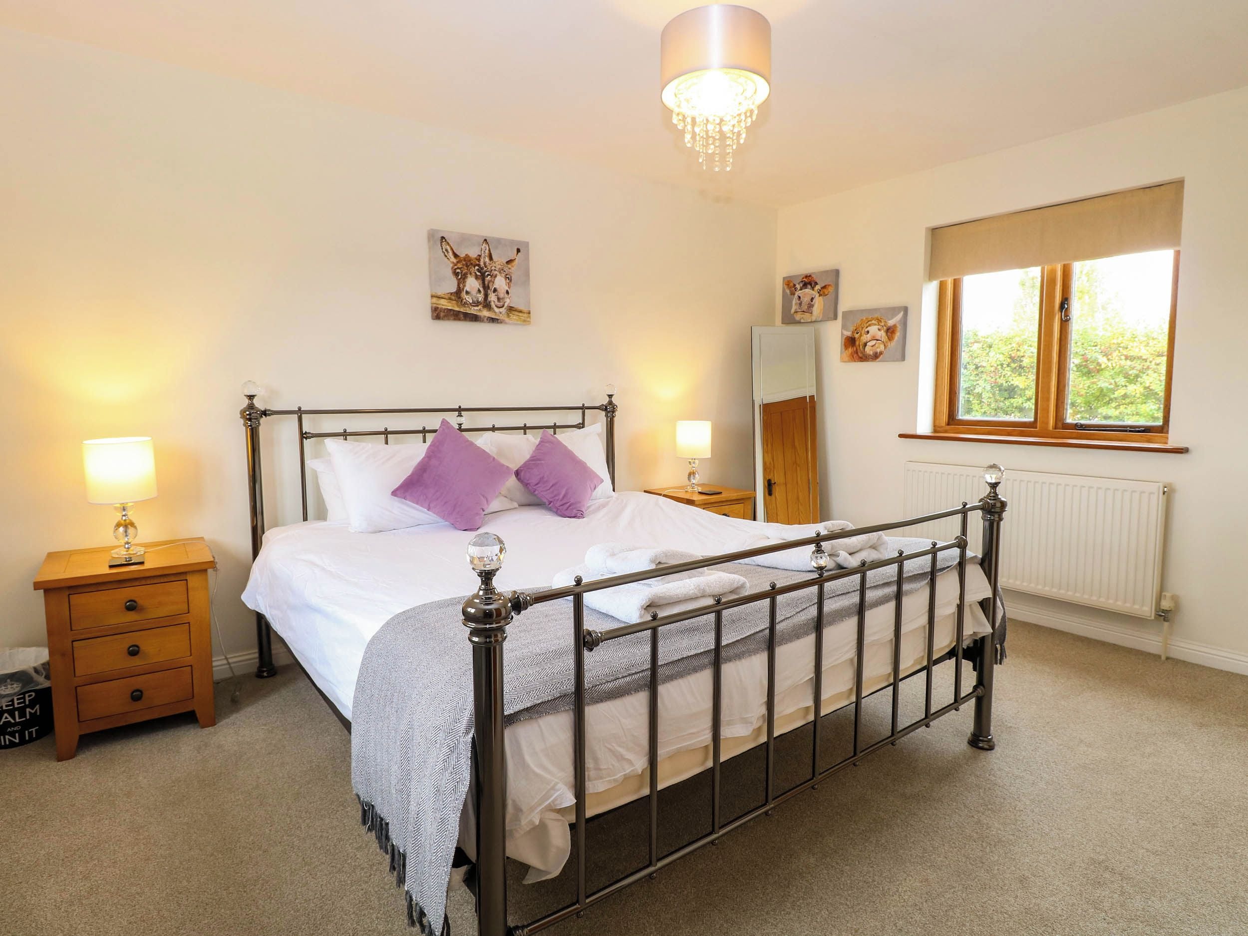 A bedroom with a metal-framed bed, two bedside tables with lamps, a window with a view, and a chandelier.
