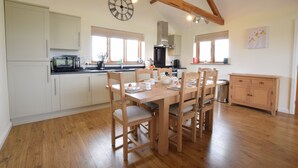 Una cocina amplia con piso de madera, armarios blancos y un comedor con mesa y sillas de madera.