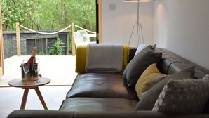A modern living room with a leather sofa, a small round table with a champagne bottle and glasses, and a large floor lamp. - Red Poll Barn (Halesworth)