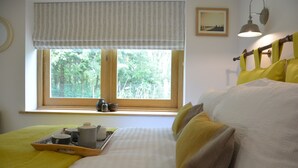 A bedroom with a large window, a bedside table with a tray of breakfast items, and a bed with yellow pillows. - Red Poll Barn (Halesworth)