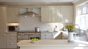 A modern kitchen with white cabinetry, a stove, oven, microwave, and a bowl of apples on the counter. - Meadowsweet, Blythburgh (Halesworth)