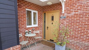 A brick house with a wooden door, a small garden area with a table and chairs, and a potted plant. - Meadowsweet, Blythburgh (Halesworth)