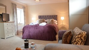 A bedroom with a large bed, bedside lamps, a television on a dresser, and a coffee maker on the nightstand. - Meadowsweet, Blythburgh (Halesworth)