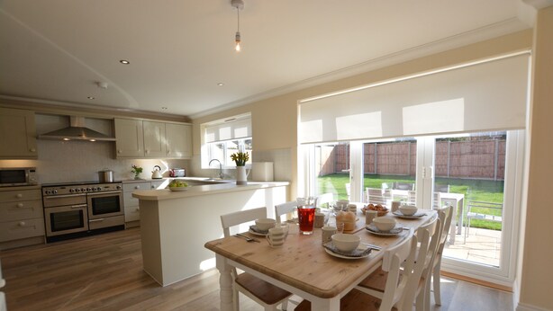 A modern kitchen with white cabinetry, a wooden dining table, and a view of the backyard through large windows. - Meadowsweet, Blythburgh (Halesworth)