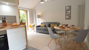 A modern kitchen with a dining area, a grey sofa with yellow cushions, and a dining table with chairs. - Milk Parlour (Halesworth)