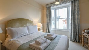 A hotel room with a large bed, a desk, and a window with curtains. - Walton House, Southwold (Reydon)