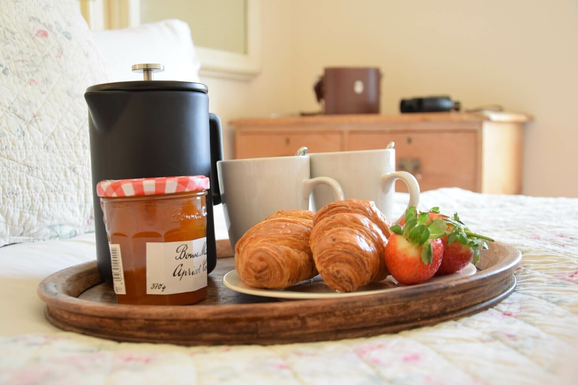 A tray with a jar of jam, croissants, and strawberries on a bed.