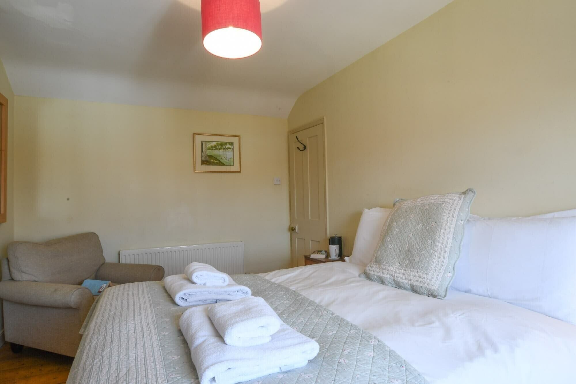 A hotel room with a bed, a chair, a radiator, a door, and a framed picture on the wall.