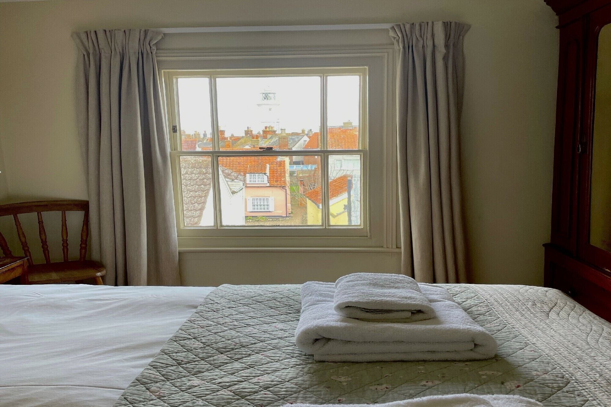 A room with a bed, a window with curtains, and a view of buildings outside.