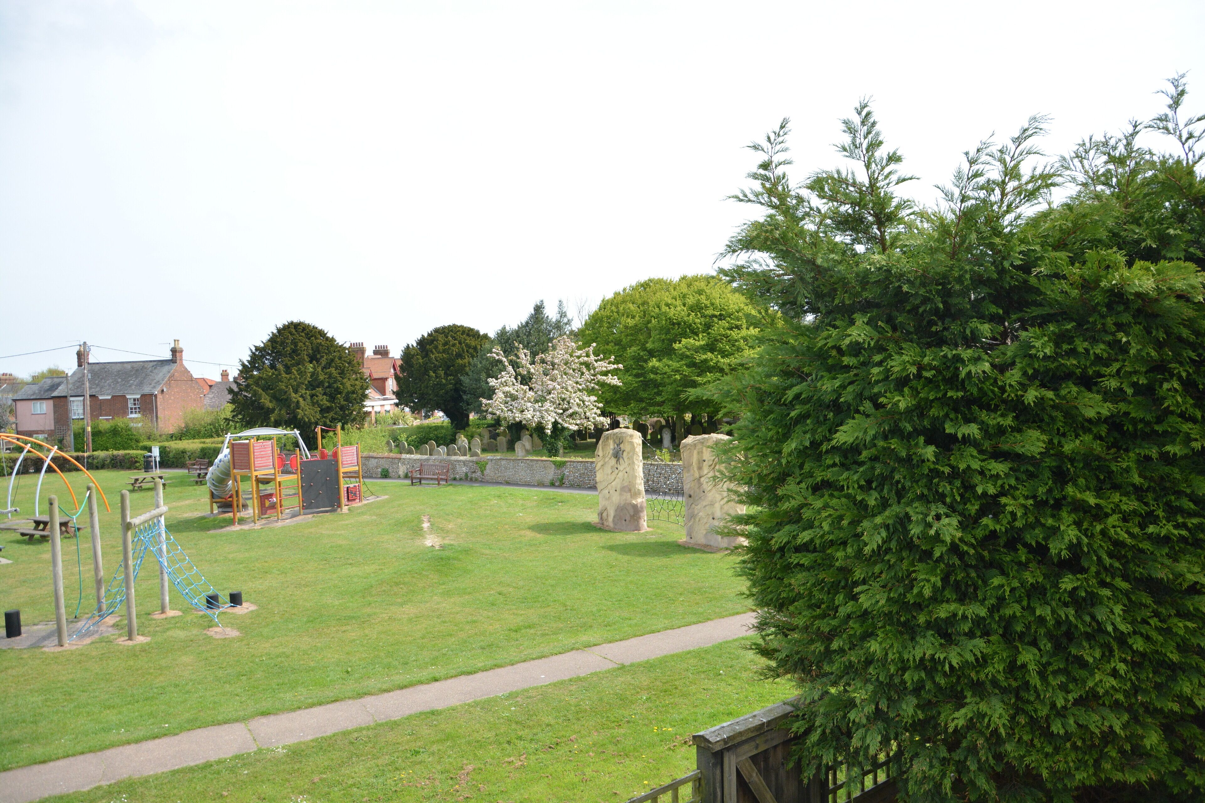 A park with playground equipment, a grassy area, and a stone wall.