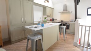 A modern kitchen with light wood cabinets, a central island, and a hanging pendant light. - Badminton, Thorpeness (Leiston)