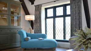 A room with a blue sofa, a wooden table with a plant, a lamp, and a window with curtains. - Badminton, Thorpeness (Leiston)