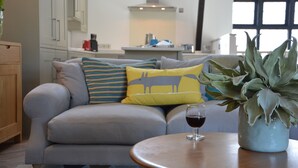 A modern living room with a grey sofa, a round wooden coffee table, and a potted plant. - Badminton, Thorpeness (Leiston)