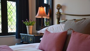 A neatly made bed with pink and white bedding, a bedside table with a lamp, and a window with curtains. - Badminton, Thorpeness (Leiston)