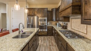 Una cocina con encimeras de granito, electrodomésticos de acero inoxidable, gabinetes de madera e iluminación colgante.