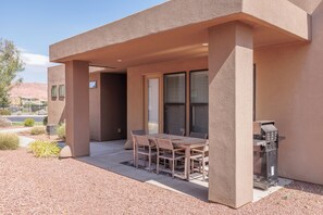 An outdoor patio with a table and chairs, a grill, and a view of the desert landscape.