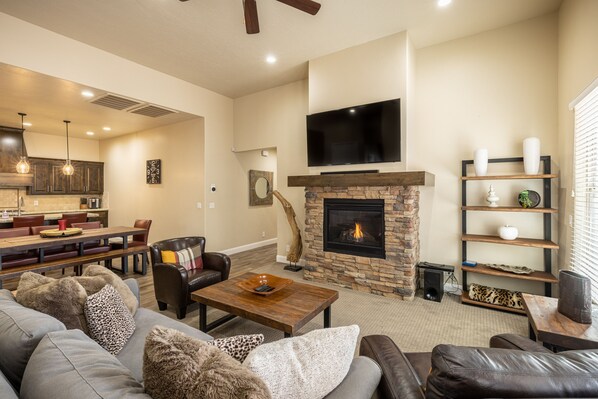 A modern living room with a fireplace, leather sofas, a dining area, and a kitchen in the background.