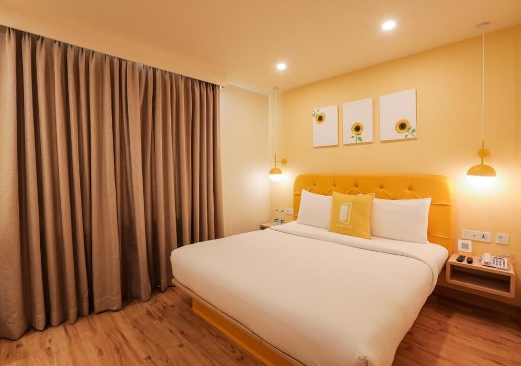 A hotel room with a large bed, curtains, a headboard with lights, a nightstand, and wall art.