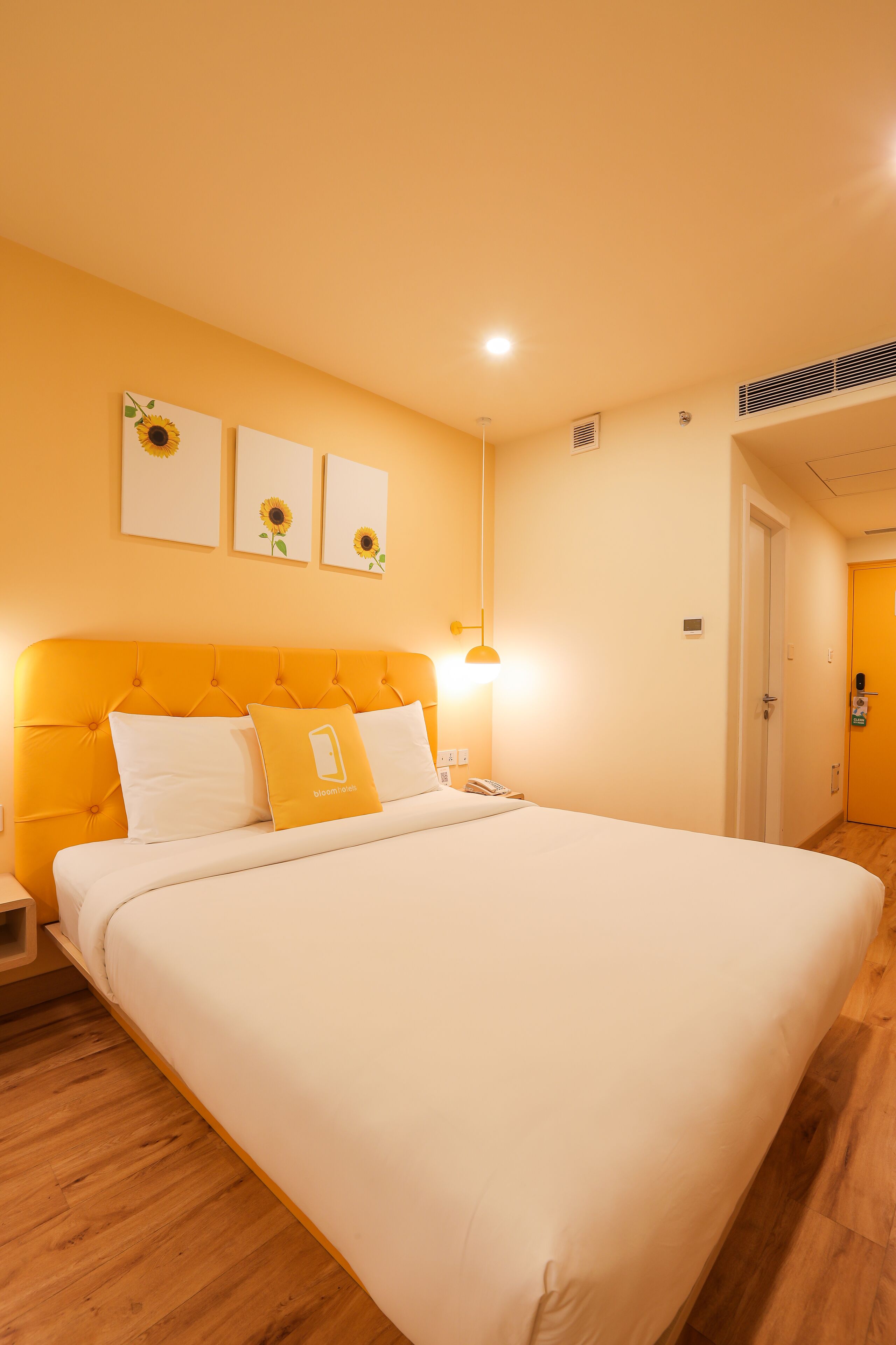 Habitación de hotel con una cama grande, una mesita de noche y un aparador. Hay tres obras de arte colgadas en la pared que representan girasoles.