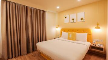 Habitación de hotel con una cama grande, suelo de madera, cabecera con un detalle amarillo y dos lámparas fijadas a la pared.