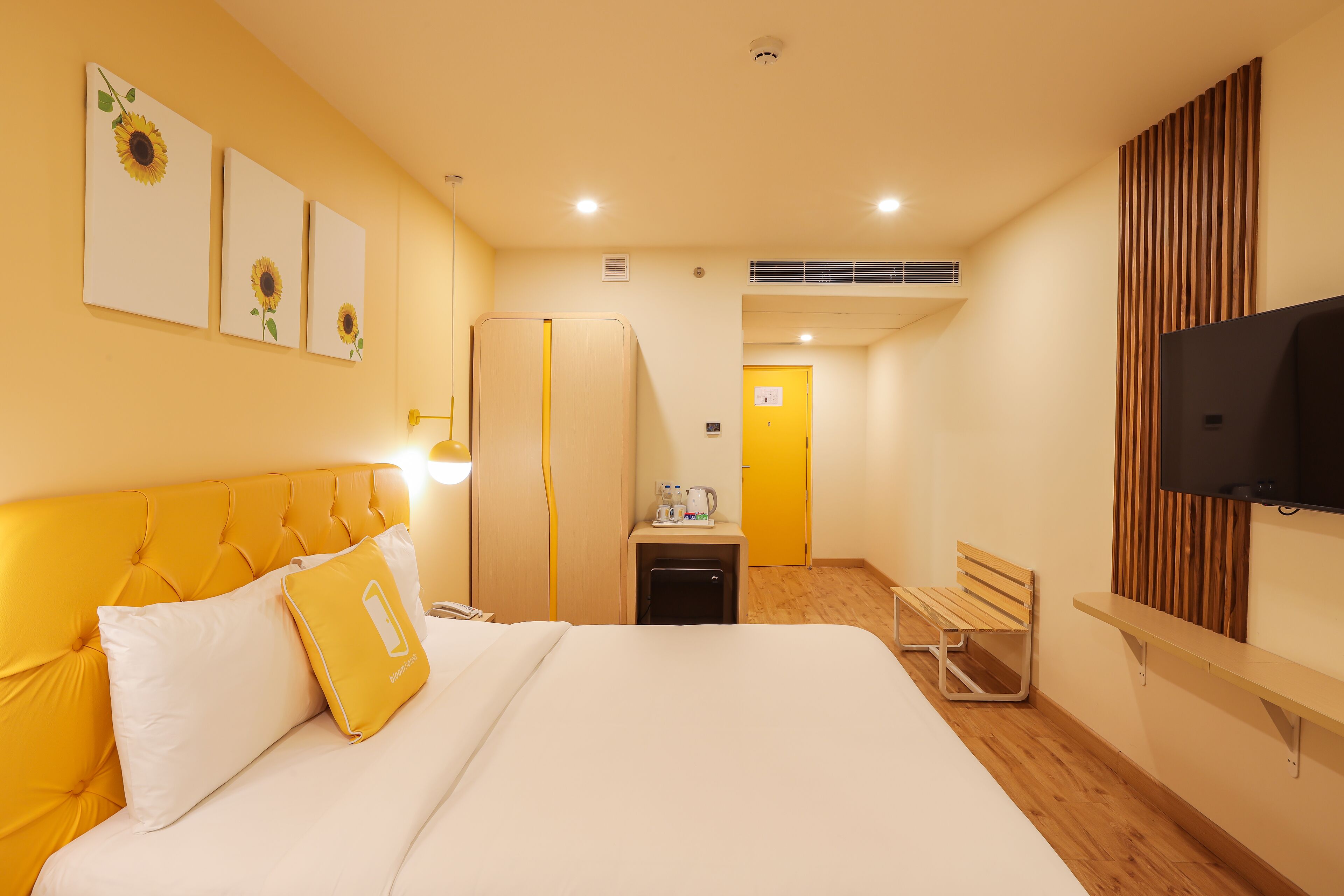 A hotel room with a bed, a desk, a chair, a TV, and artwork on the wall.