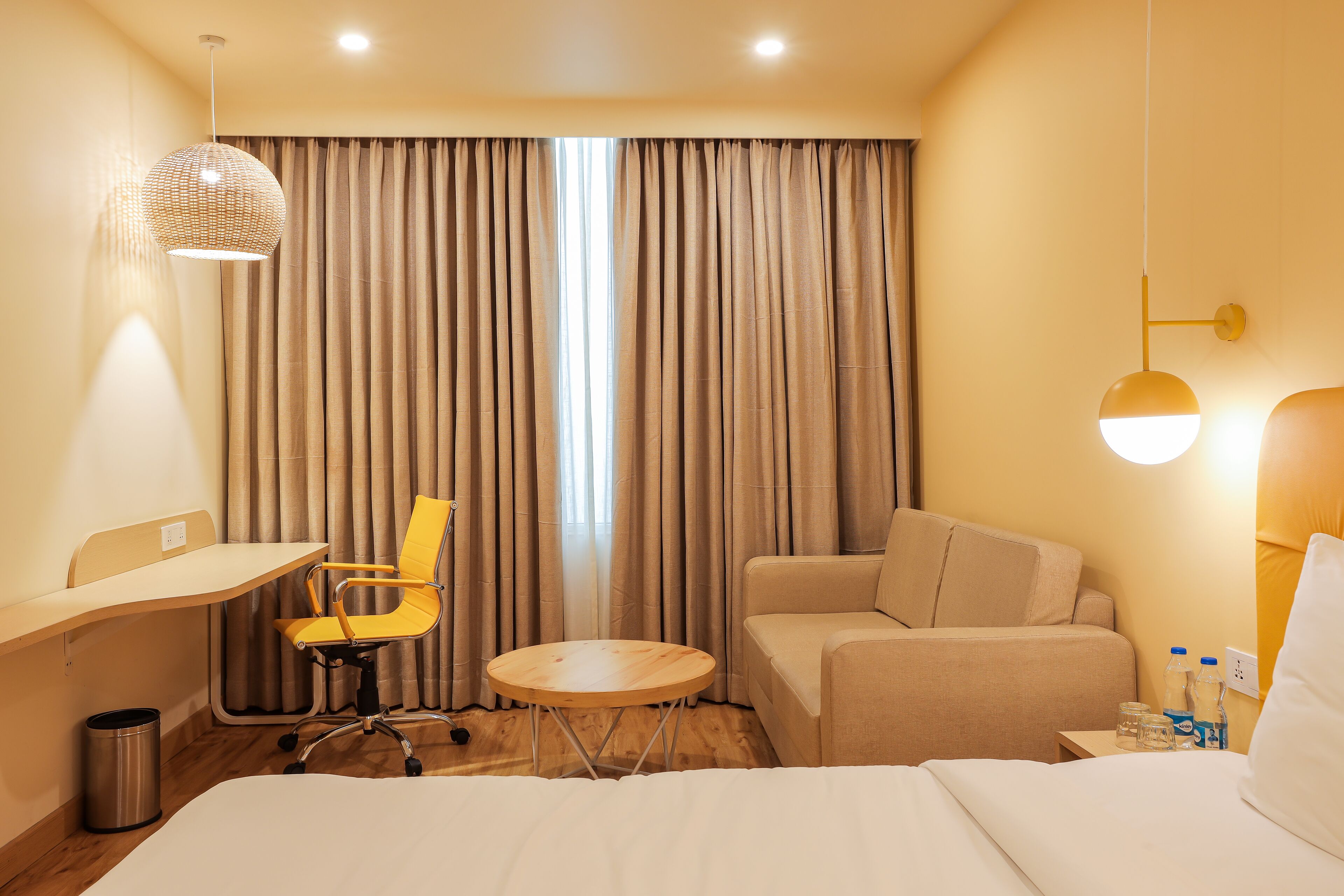 A hotel room with a bed, a desk, a chair, a small table, and a sofa.