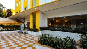 L’entrée d’un hôtel, avec un sol à carreaux, une façade jaune et blanche et un jardin bien entretenu.