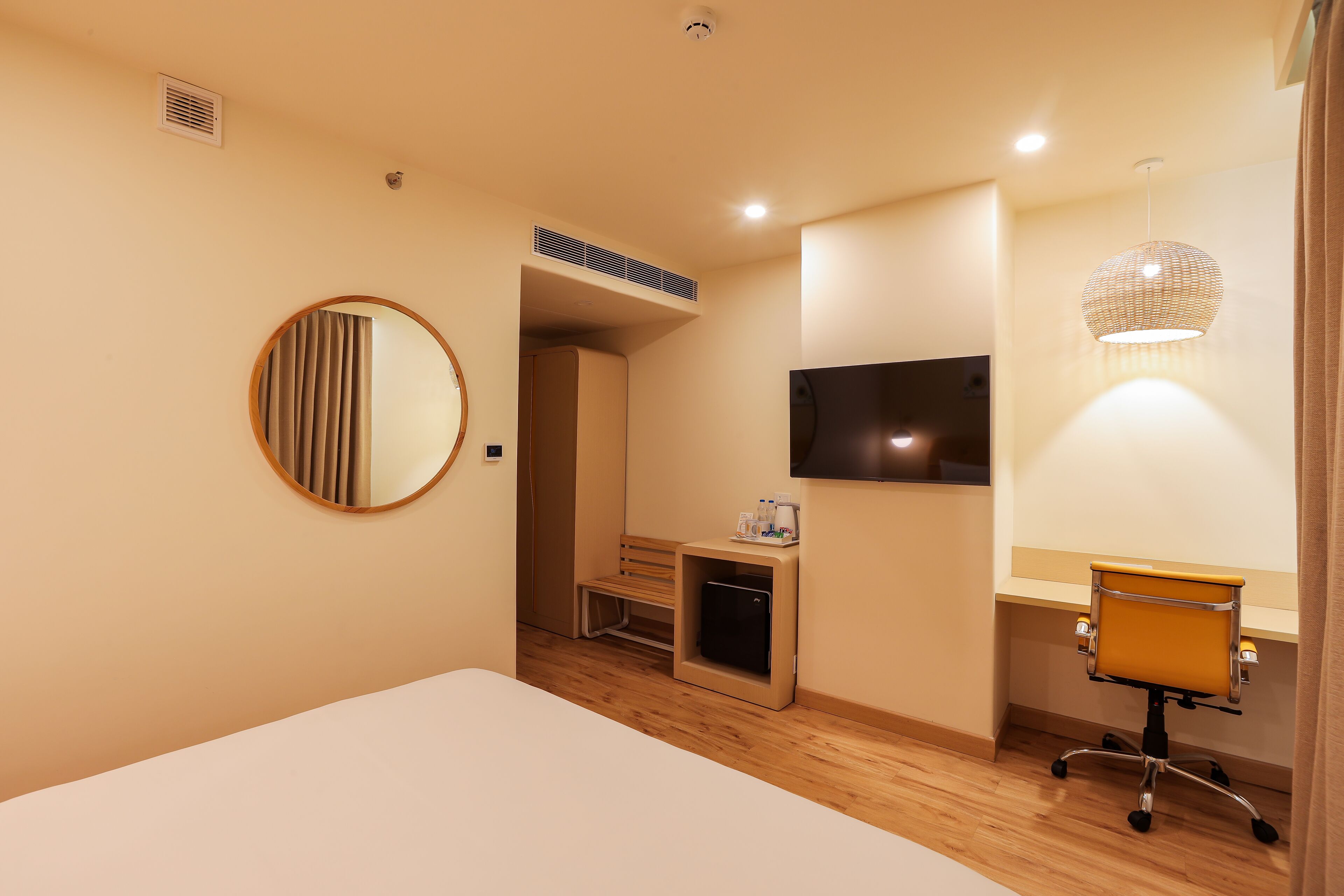 Habitación de hotel con una cama, un escritorio con silla, un televisor, un espejo y una mesita con una botella y vasos.