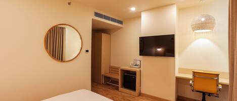 A hotel room with a bed, a desk with a chair, a television, a mirror, and a small table with a bottle and glasses.