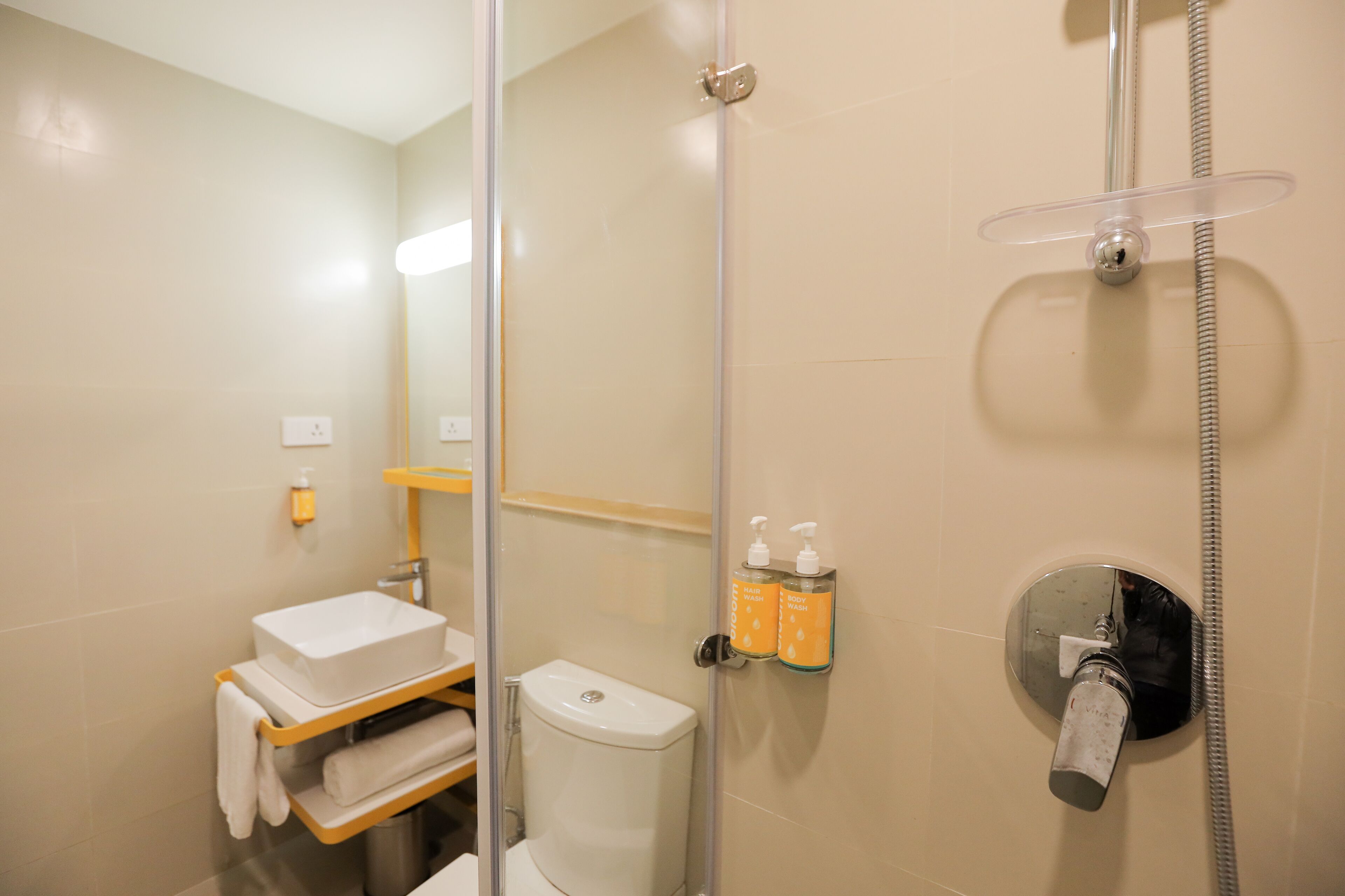 A bathroom with a glass shower enclosure, a toilet, a sink with a towel rack, and two soap dispensers on the wall.