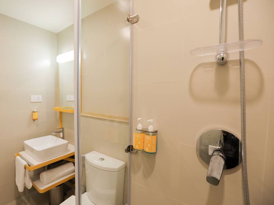 A bathroom with a glass shower enclosure, a toilet, a sink with a towel rack, and two soap dispensers on the wall.